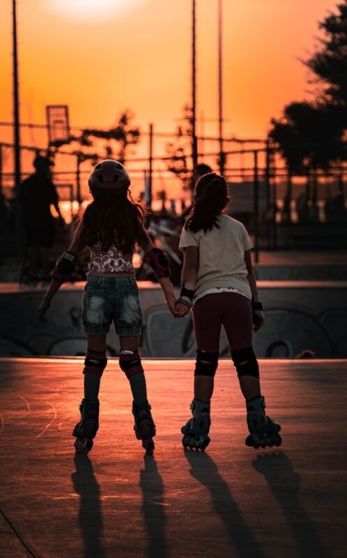Home Two girls roller skate in a scenic urban skatepark at sunset, creating a vibrant silhouette.
